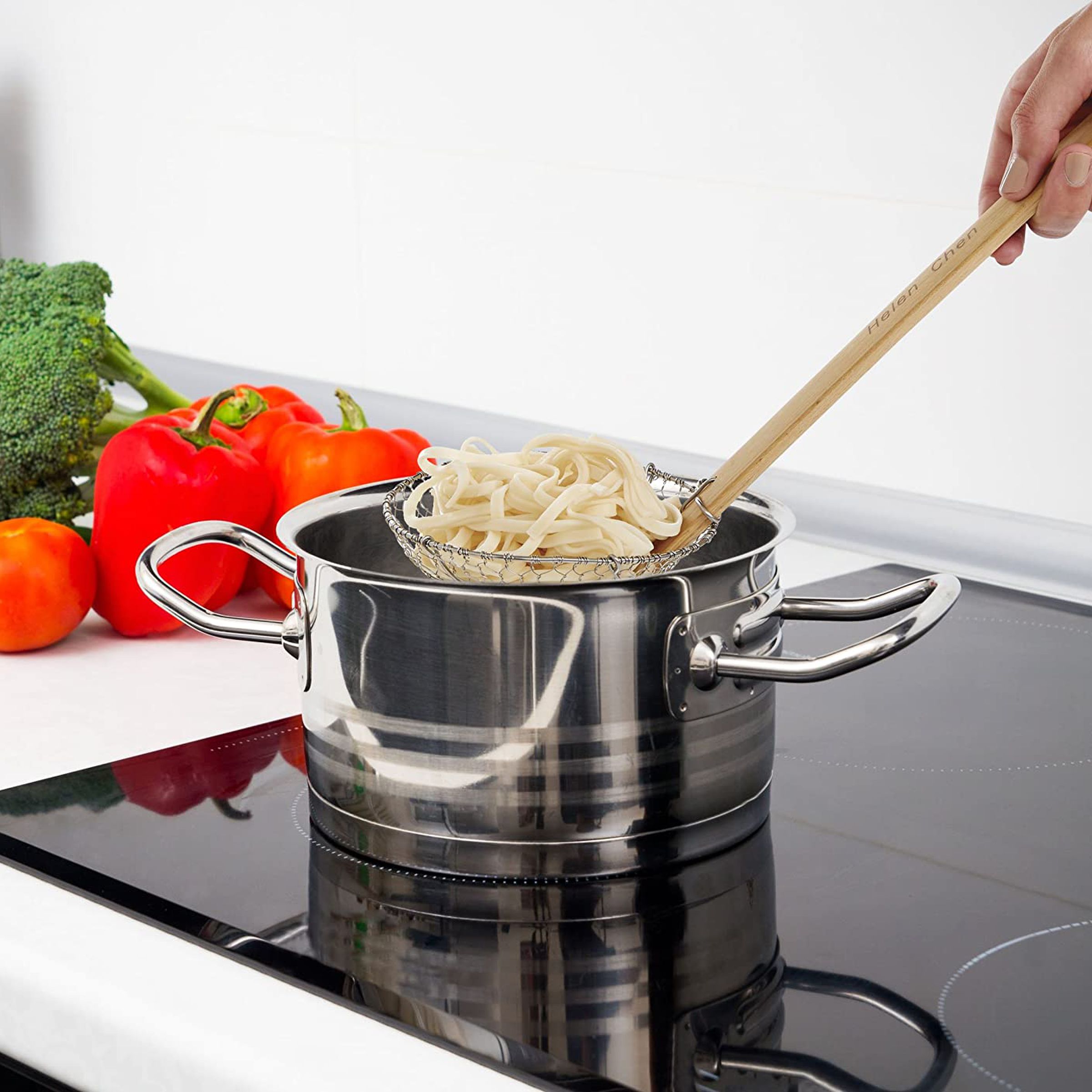 Hand fishing pasta out of a metal pot using spider spoon.