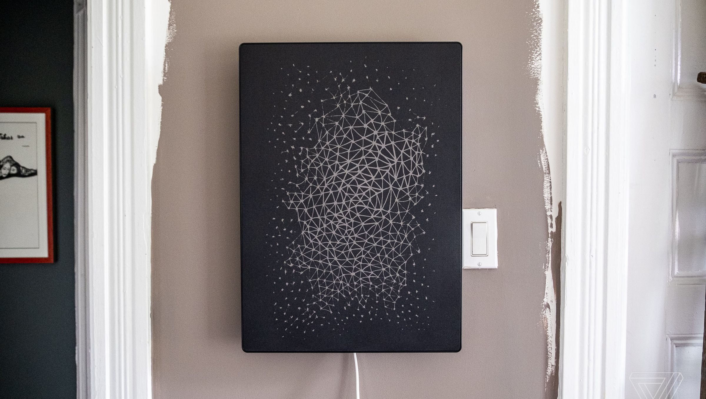 A black Ikea picture frame speaker with a geometric pattern design mounted on a wall beside a light switch.