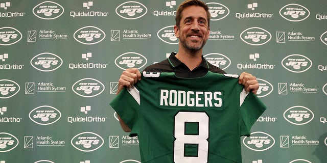 Aaron Rodgers holds jets jersey at conference