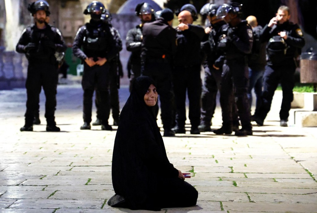 A Palestinian woman sits near Israeli border policemen in the Al-Aqsa compound, also known to Jews as the Temple Mount, while tension arises during clashes with Palestinians in Jerusalem's Old City, on April 5, 2023. 
