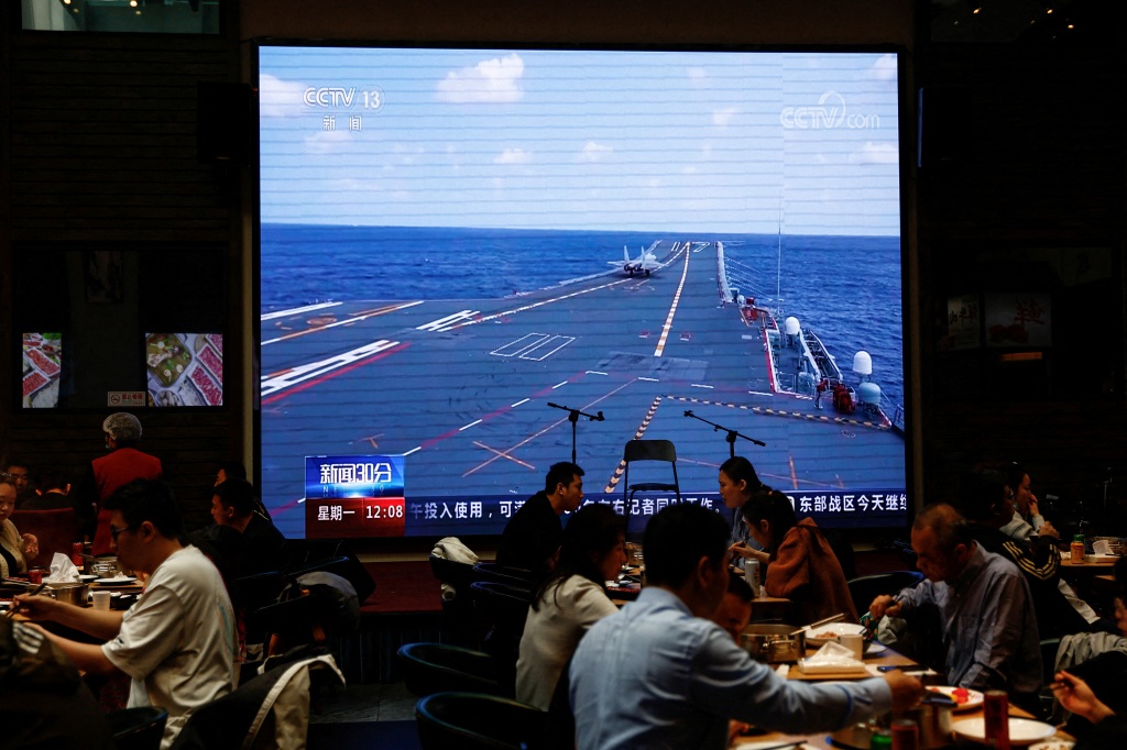 Customers dine near a giant screen broadcasting news footage of an aircraft taking off from China's Shandong aircraft carrier while taking part in a combat readiness patrol and "Joint Sword" exercises around Taiwan conducted by the Eastern Theatre Command of China's People's Liberation Army (PLA), at a restaurant in Beijing, China on April 10, 2023.