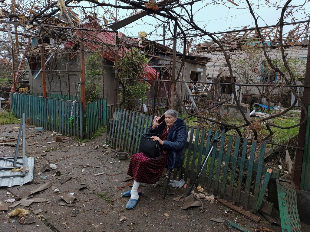 A local woman speaks on her phone as she sits on a bench next to a residential house damaged by a Russian missile strike, amid Russia's attack on Ukraine, in Mykolaiv on April 27, 2023. 