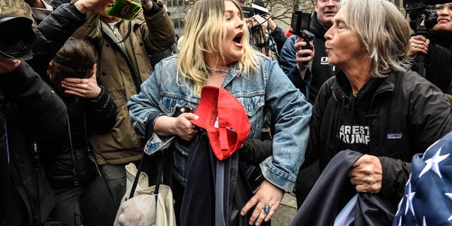 The Trump supporter engages in a verbal exchange with a protester with the words "ARREST TRUMP" on their shirt.