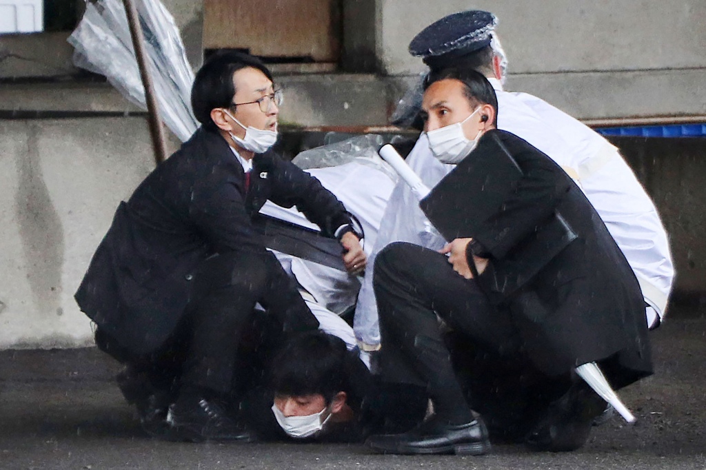 A man (bottom) is detained after throwing an apparent"smoke bomb" in Wakayama on April 15, 2023, where Japan's Prime Minister was due to give a speech.