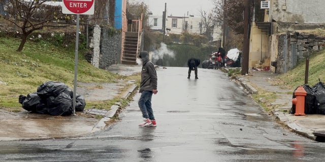 An addict stands in the middle of the street slumped over, struggling to remain upright.