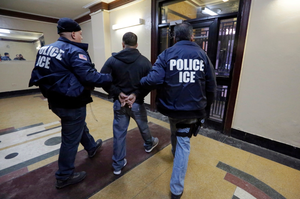 Immigration and Customs Enforcement officers escort an arrestee in an apartment building, in the Bronx borough of New York, during a series of early-morning raids.