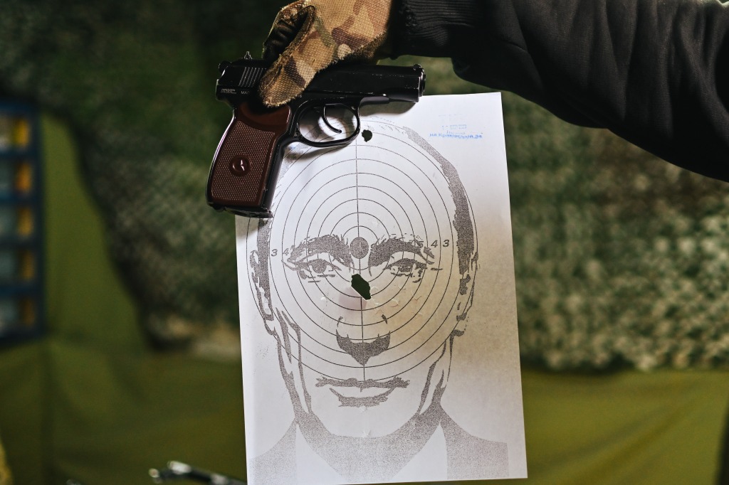 Andriy, the owner of the shooting range, holds a target with Putin's face with a hit right in the middle and a dummy gun above it in Lviv, Ukraine. 