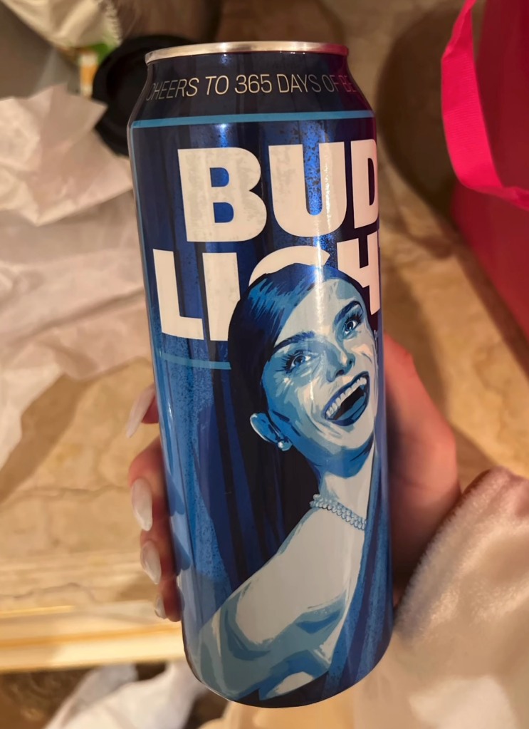 Hand holding blue Bud Light beer can with an illustration of Dylan Mulvaney's face on it