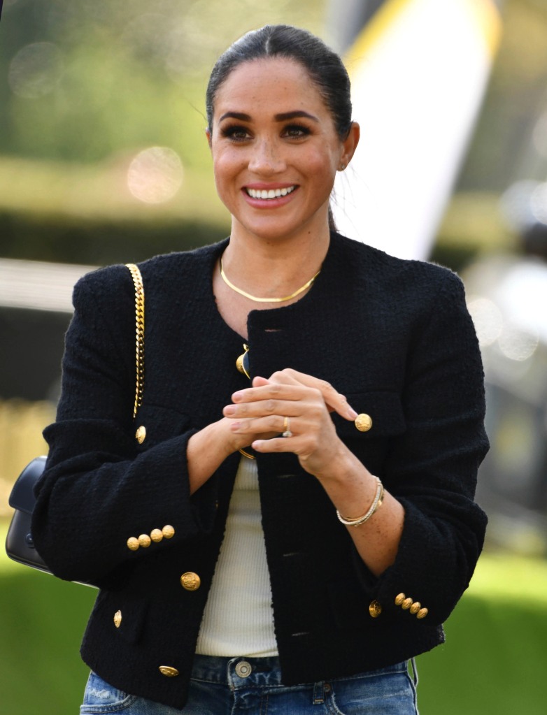 Meghan Markle smiling and clasping her hands together. 