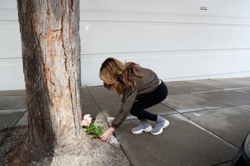 A woman lays flowers by a tree near the area outside of the building where tech executive Bob Lee was stabbed to death
