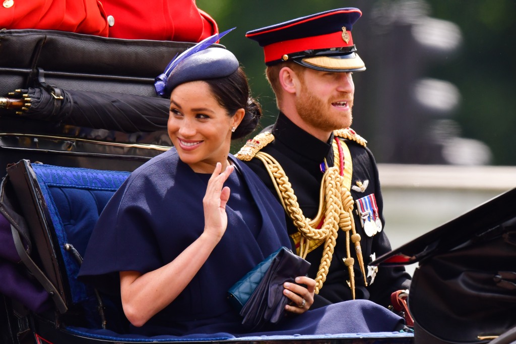 Prince Harry and Meghan Markle in a royal motorcade, waving from a car. 
