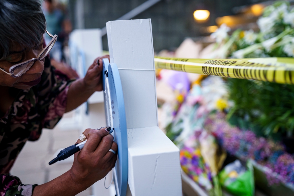 Manetta Lemkheitir writes on a cross at the memorial outside of the Old National Bank on Tuesday.