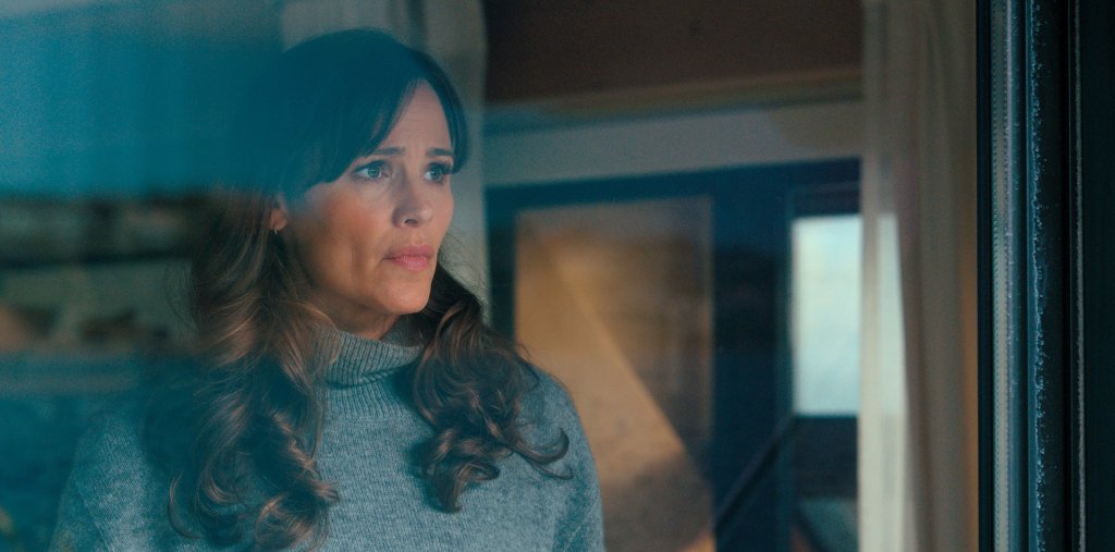 Jennifer Garner looks out a window, looking worried. 