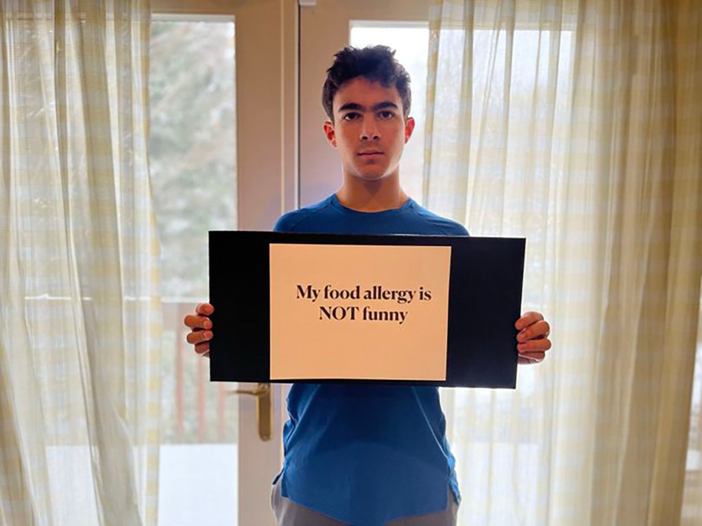 Mandelbaum's son holding a sign that reads, "My food allergy is NOT funny"