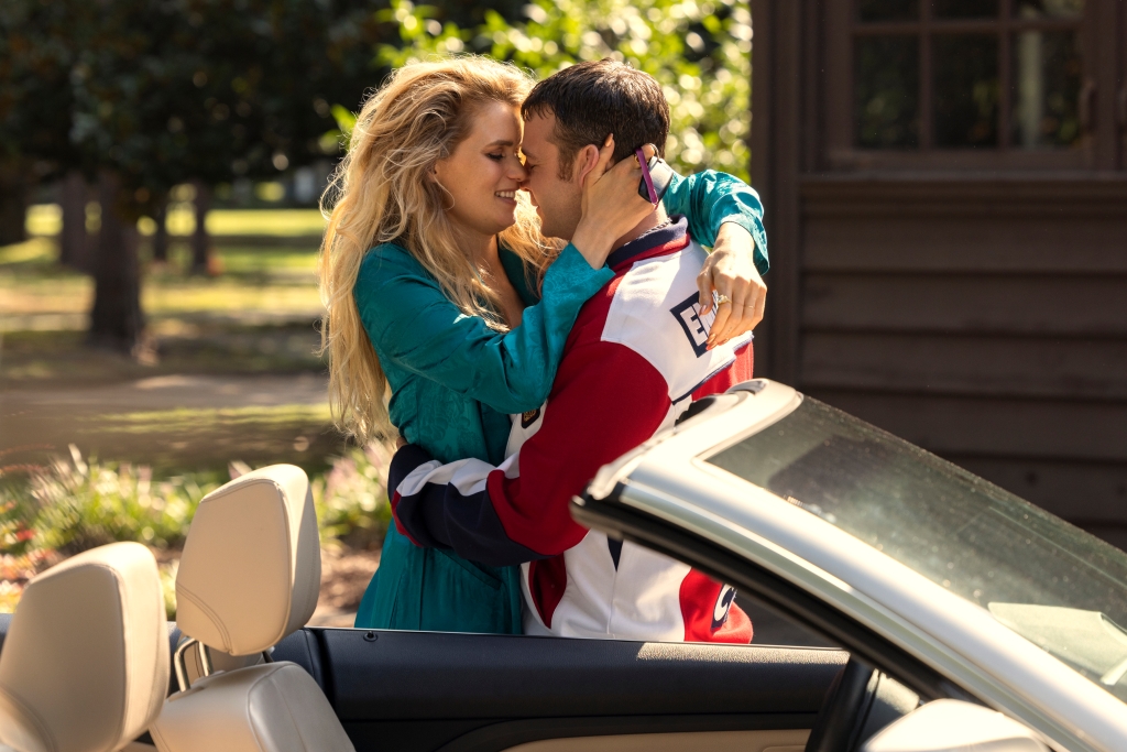 Abbey Lee and Emory Cohen kiss standing outside in front of a car. 