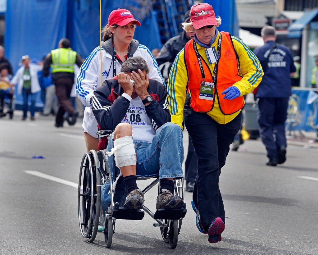 An injured man with his face in his hands is wheeled away from the aftermath of explosions at the finish line of the Boston Marathon on Monday, April 15, 2013. 