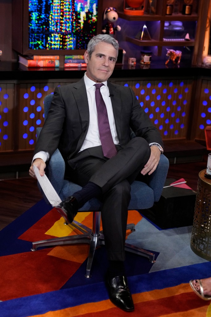 Andy Cohen sitting on a chair smiling at the camera. 
