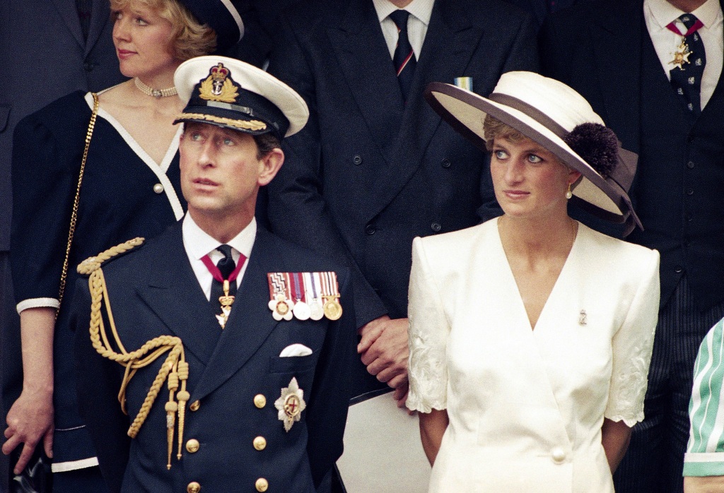 Prince Charles and Princess Diana sitting next to each other looking serious while he wears a uniform and she's in white. 