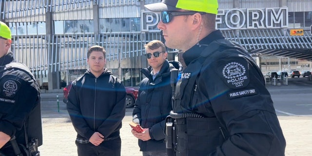 Nathaniel Pawlowski, second from right, holds a Bible and stands with friend Deklan Friesen while officers detain them.