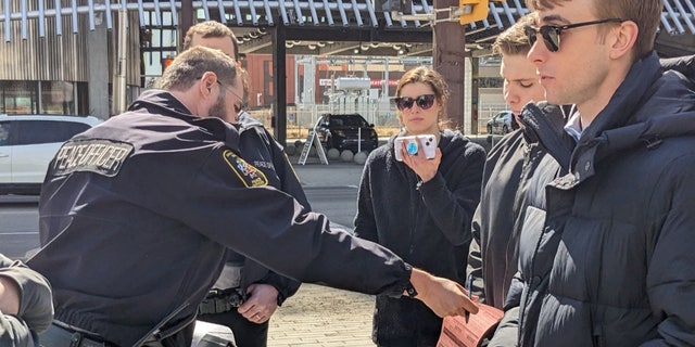 An officer issues a ticket to Deklan Friesen for allegedly violating a municipal bylaw by preaching outside a public library.