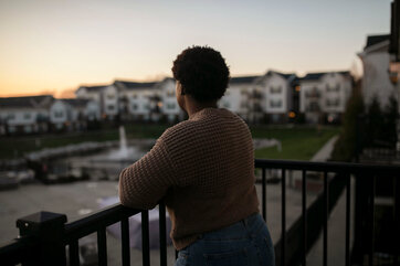 D., shown from behind so that her face is obscured, looking out over a balcony.