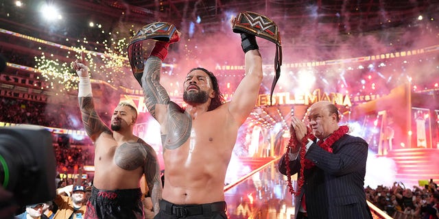 Roman Reigns, center, holds up his WWE heavyweight and universal championship belts after defeating Cody Rhodes in the main event of WrestleMania 39, Sunday, April 2, 2023 at SoFi Stadium in Inglewood, California.