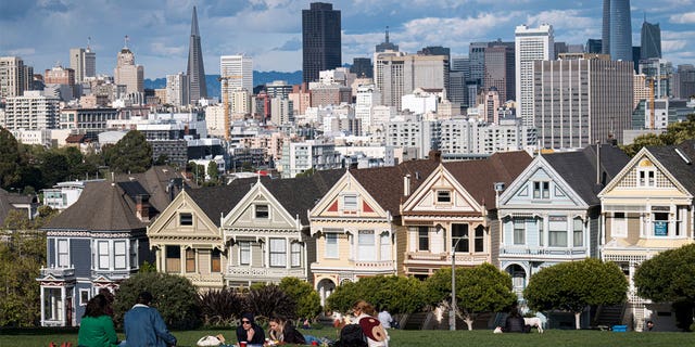 People sit in Alamo Square overlooking the city skyline in San Francisco, California, U.S., on Thursday, March 26, 2020. Governor Newsom on March 19 ordered that all of the state's 40 million residents go into home isolation while saying outdoor activity is permissible with proper social distancing. Several parks reported a surge in visitors over the weekend from people wanting to get out of the house. 