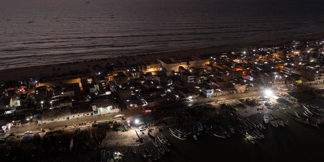 An offshore gas terminal is lit up amid the Atlantic Ocean as houses lay on the beachfront between the sea and the Senegal River, bottom, in Saint Louis, Senegal, on Jan. 18, 2023.