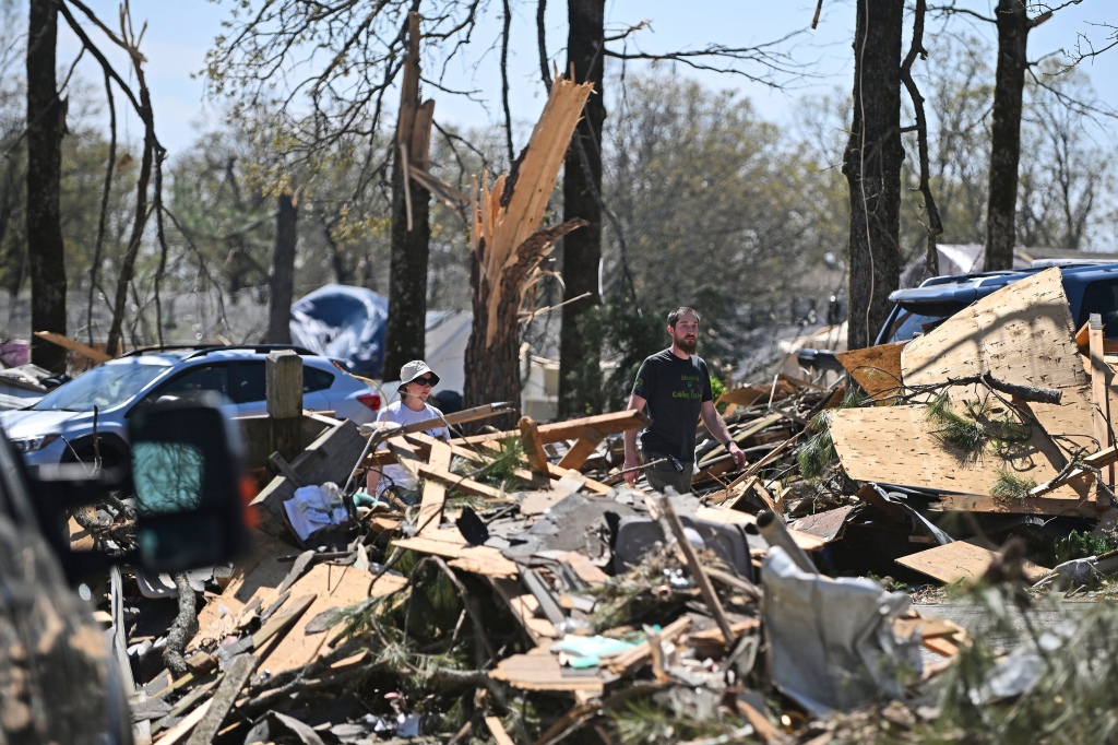 People walk beside piles of debris on April 2, 2023, in the Indian Hills area of North Little Rock, Ark. 