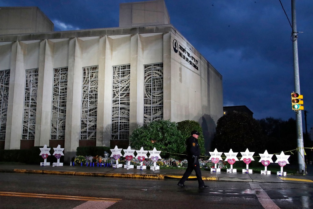 A Pittsburgh Police officer walks past the Tree of Life Synagogue and a memorial of flowers and stars in Pittsburgh on Sunday, Oct. 28, 2018, in remembrance of those killed and injured when a shooter opened fire during services Saturday at the synagogue.