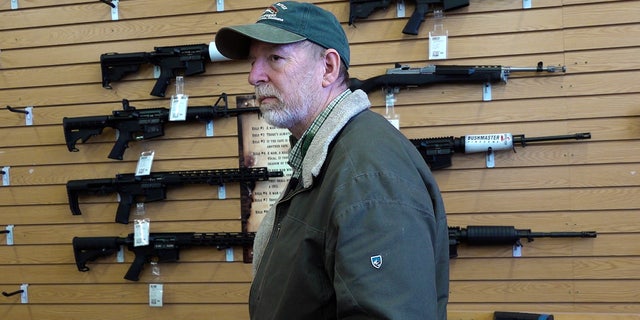 Gun store manager Bruce Smith stands in front of semiautomatic rifles hanging on the wall