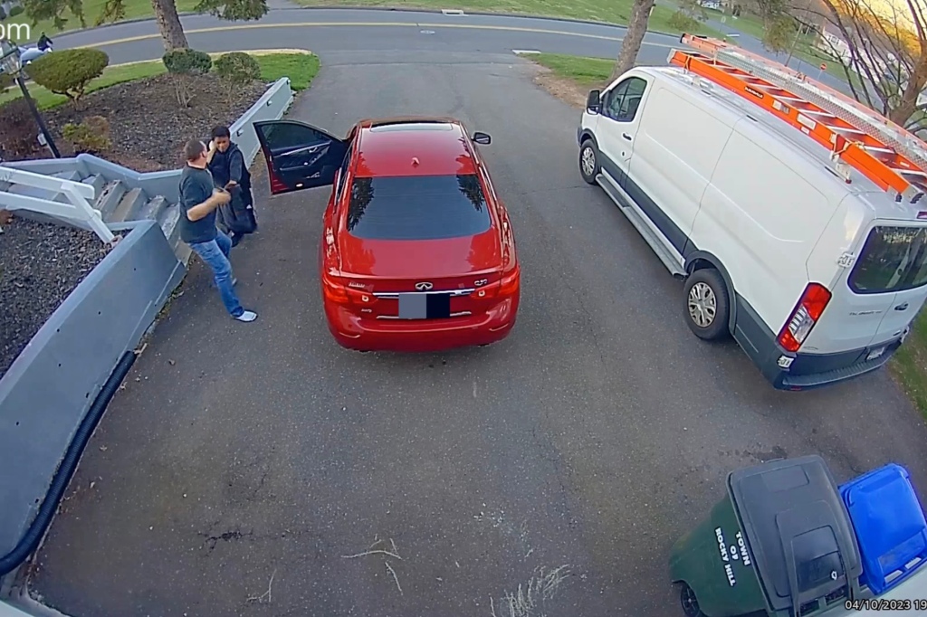 The footage shows a man jogging into the driveway from the street, with a cell phone to his ear, as he opens the door of a parked red car.