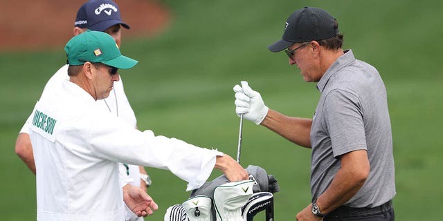 Phil Mickelson of the United States talks with his caddie Tim Mickelson warms up on the practice areaduring a practice round prior to the 2023 Masters Tournament at Augusta National Golf Club on April 4, 2023 in Augusta, Georgia.