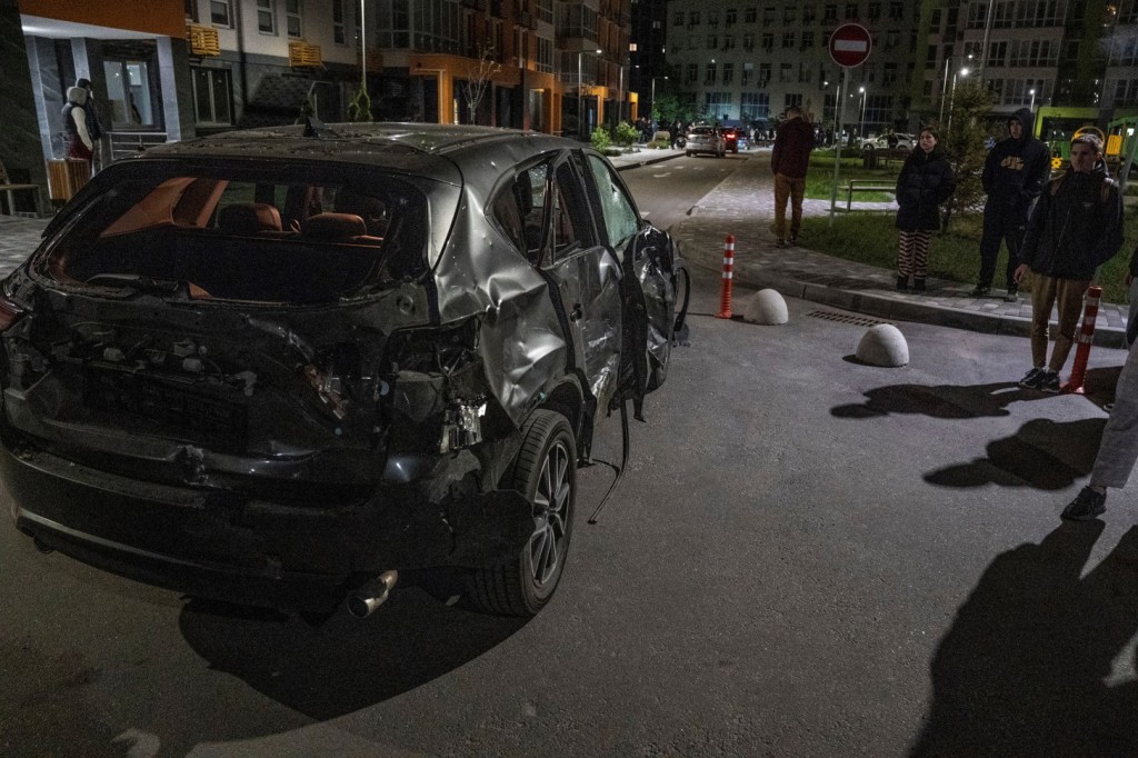 Local residents stand next to a car damaged by the remains of a suicide drone in Kyiv, Ukraine on May 8, 2023.