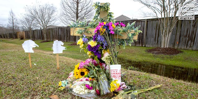 A small wooden cross covered with flowers by the side of a highway