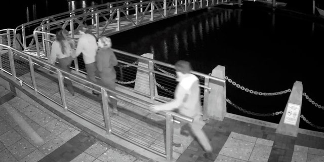 Black and white surveillance video showing young people on a dock at night