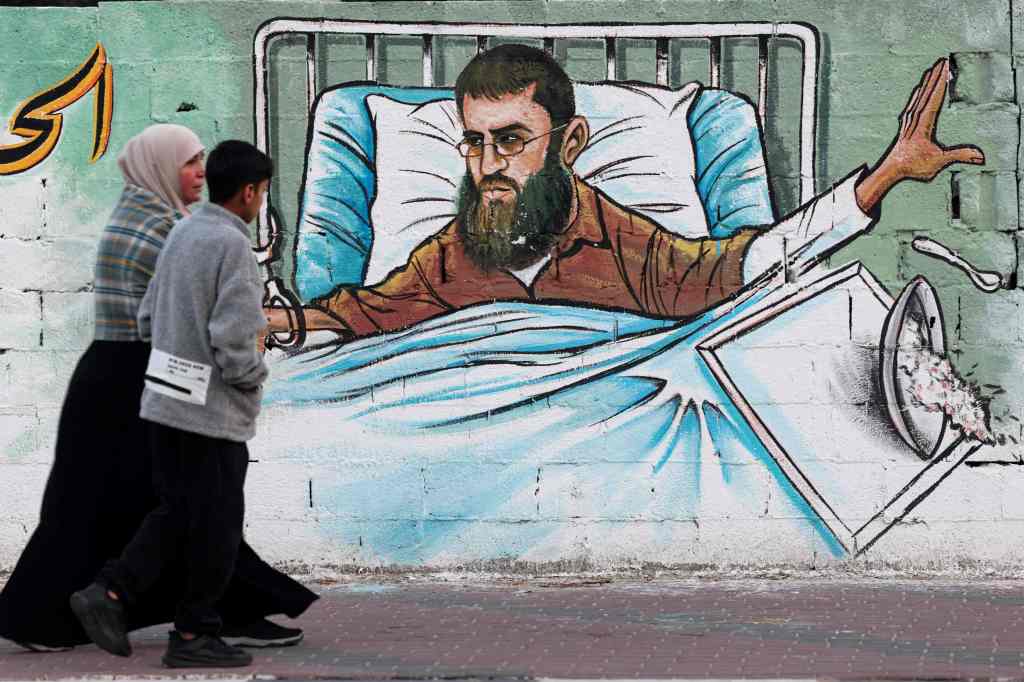 A Palestinian woman and her son walk past a mural depicting Khader Adnan in Gaza City on May 2, 2023. 