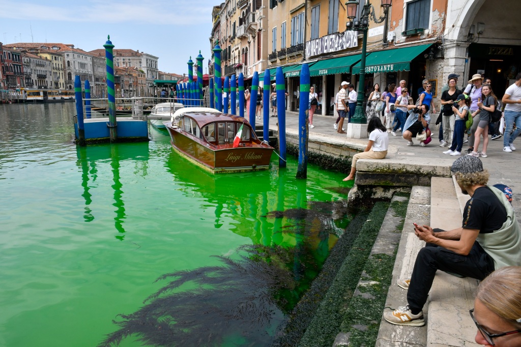 A gondola navigates along Venice's historical Grand Canal as a patch of phosphorescent green liquid spreads in it.