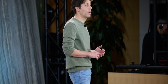 Sam Altman standing in green shirt, jeans