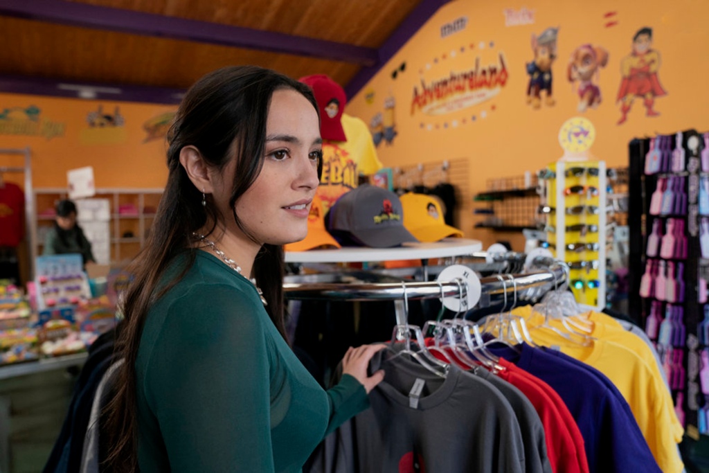 Chase Sui Wonders, Pete Davidson's real-life girlfriend. She's in a clothing store with her hand on a rack of shirts and is looking at someone off-camera. She's smiling slightly.