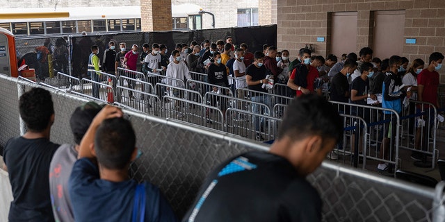 Migrants standing at a fence for a bus