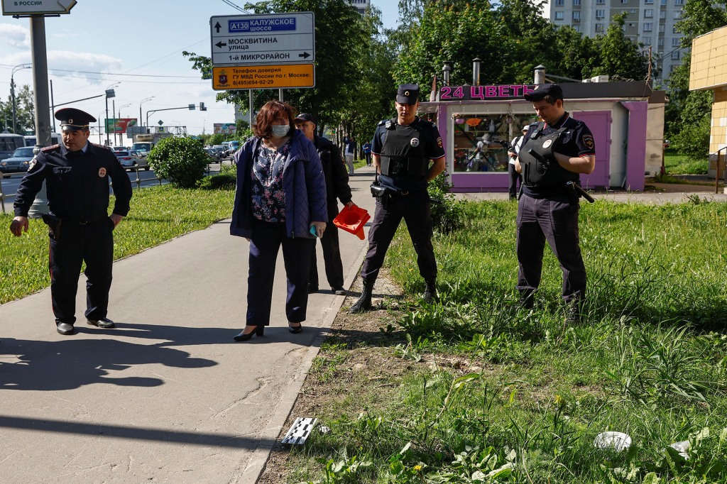 People, including Russian law enforcement officers, stand in a street during evidence gathering near a damaged multi-storey apartment block following a reported drone attack in Moscow, Russia, May 30, 2023.