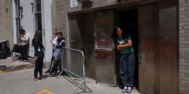 People stand by the door of a former NYPD police academy, where new immigrants to the city are being temporarily housed