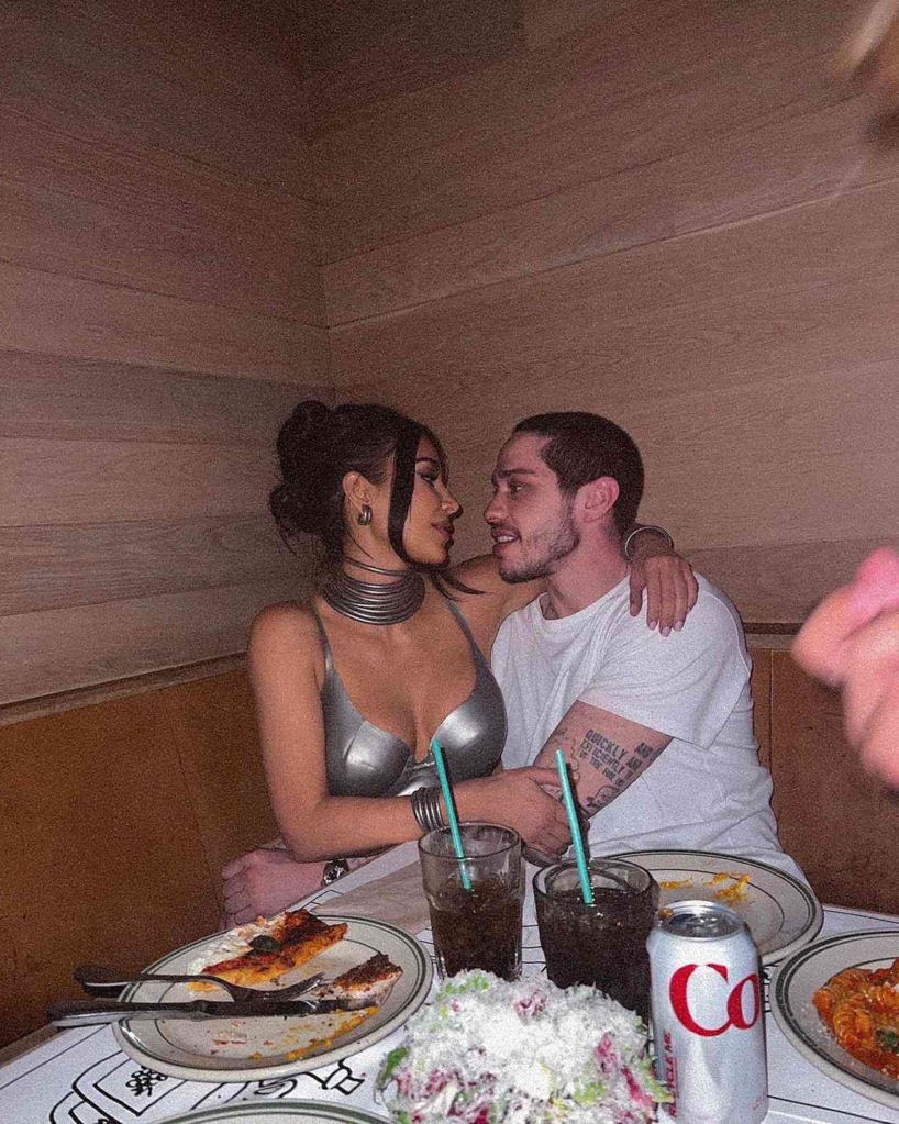 Pete Davidson and Kim Kardashian cuddling in a booth with plates in front of them. 