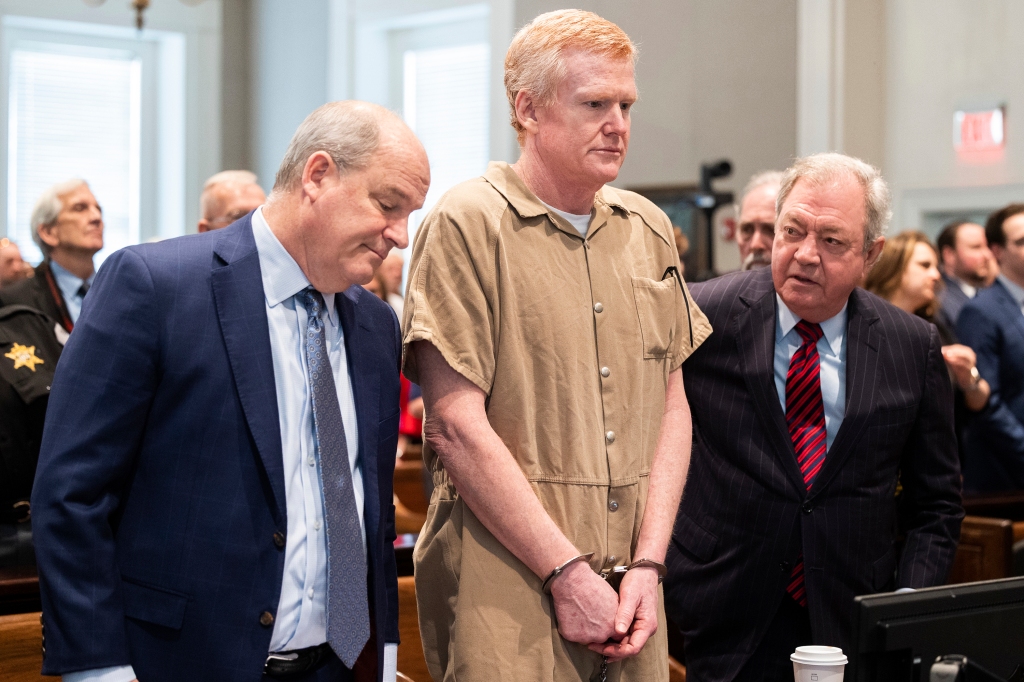 Alex Murdaugh in a tan prison jumpsuit with his hands cuffed in front of him stands between his lawyers at his sentencing hearing