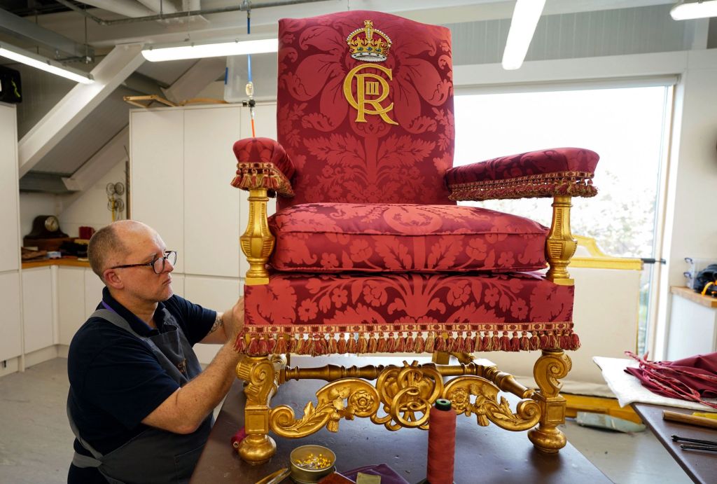 Man with glasses looking at royal looking red and gold chair.