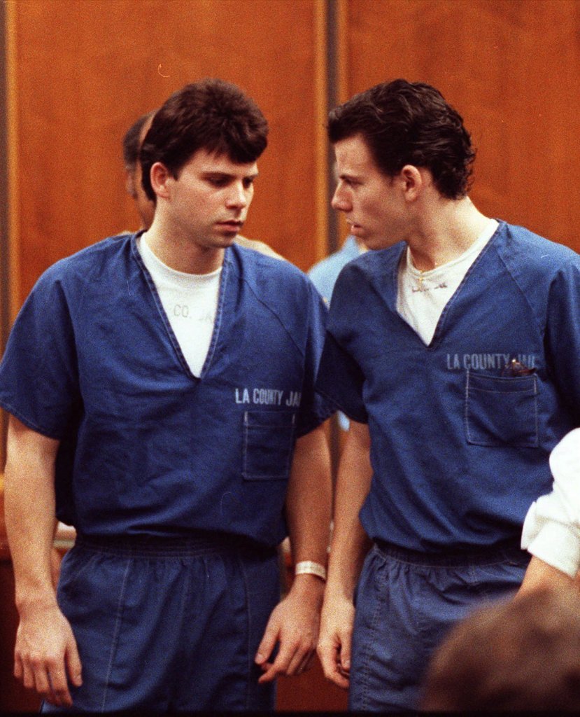 Lyle, left, and Erik Menendez in court during their trial for killing their parents. They look at each other wearing blue uniforms. 