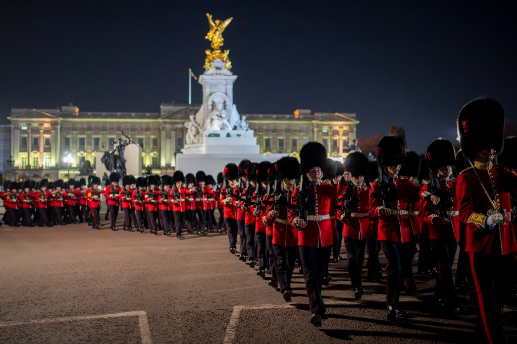 Members of the military march with Buckingham Palace in the background.