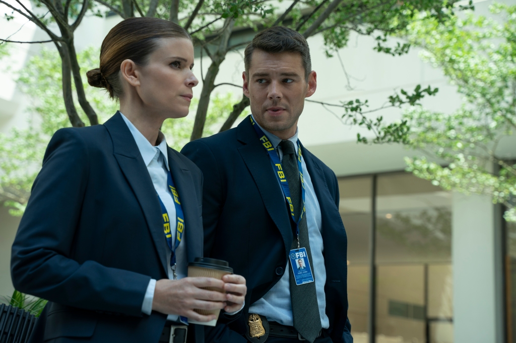 Kate Mara and Brian J Smith wearing blazers standing together talking outside of an office building. 