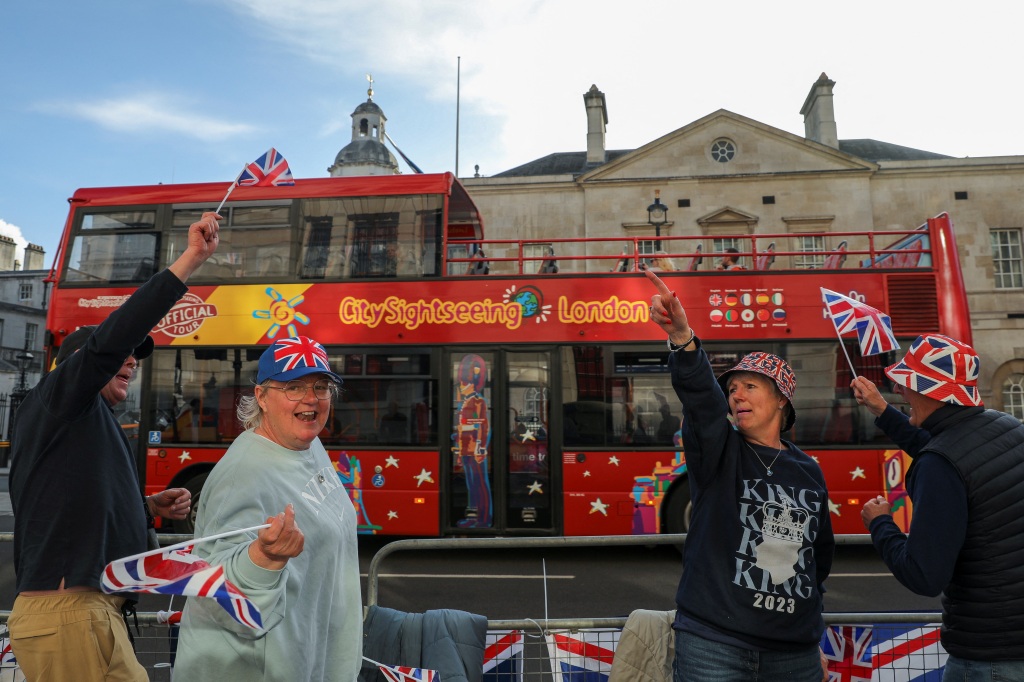 Red double-decker  sightseeing London bus with women wearing hats with the union jack on it.